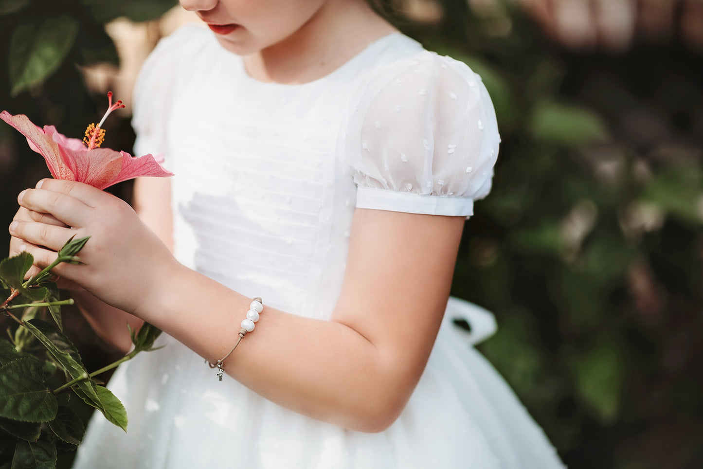 A young girl is wearing our Swiss Dot Party Dress. The elegant white dress has puff sleeves and a white lace trim on the hem.