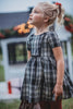 A young girl stands dressed in a black and white vintage plaid dress. The dress is mid thigh length and a sewn in pettiskirt add fullness to the bottom of the dress.