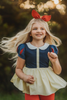 A young girl is wearing the Snow White Peplum top.  The top has a white peter pan collar and red and blue puff sleeves.  The navy blue bodice has a yellow accent and leads into a light yellow peplum skirt.  There is tulle under with a cotton liner to add fullness. 