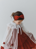 A young girl is wearing a red dress with a white tulle cape adorned with embroidered red roses. The floral details of her ensemble are striking.  The shades of red and green are the perfect addition  to our Red Rose Princess Collection.