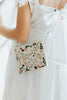 Close-up of a child in a white wedding dress holding a beaded crossbody flower girl bag with gold embroidery and pink flowers