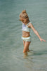 Girl wearing mint green mermaid swimsuit with purple seashell top and gold waistband, standing at the shoreline in fun sunglasses

Mermaid-themed ruffle bikini for girls with shell applique and scale print bottoms, styled for beach photos and play

Child in seafoam green two-piece swimsuit with frilly straps and shell detail, posing on sandy beach in sunshine