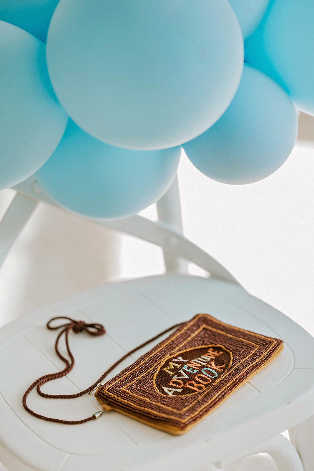 Hand-beaded “My Adventure Book” purse inspired by the Disney Pixar film Up, styled with blue balloons, ideal for birthday parties, travel lovers, or whimsical adventure gifts.

Close-up of beaded crossbody bag reading “My Adventure Book” with colorful letters and brown background, styled on a white chair with Up-themed blue balloons.

Up movie–inspired purse with rope strap and zipper closure, designed to look like Ellie and Carl’s scrapbook, perfect for fans of Pixar, Disney trips, or birthday gifts.