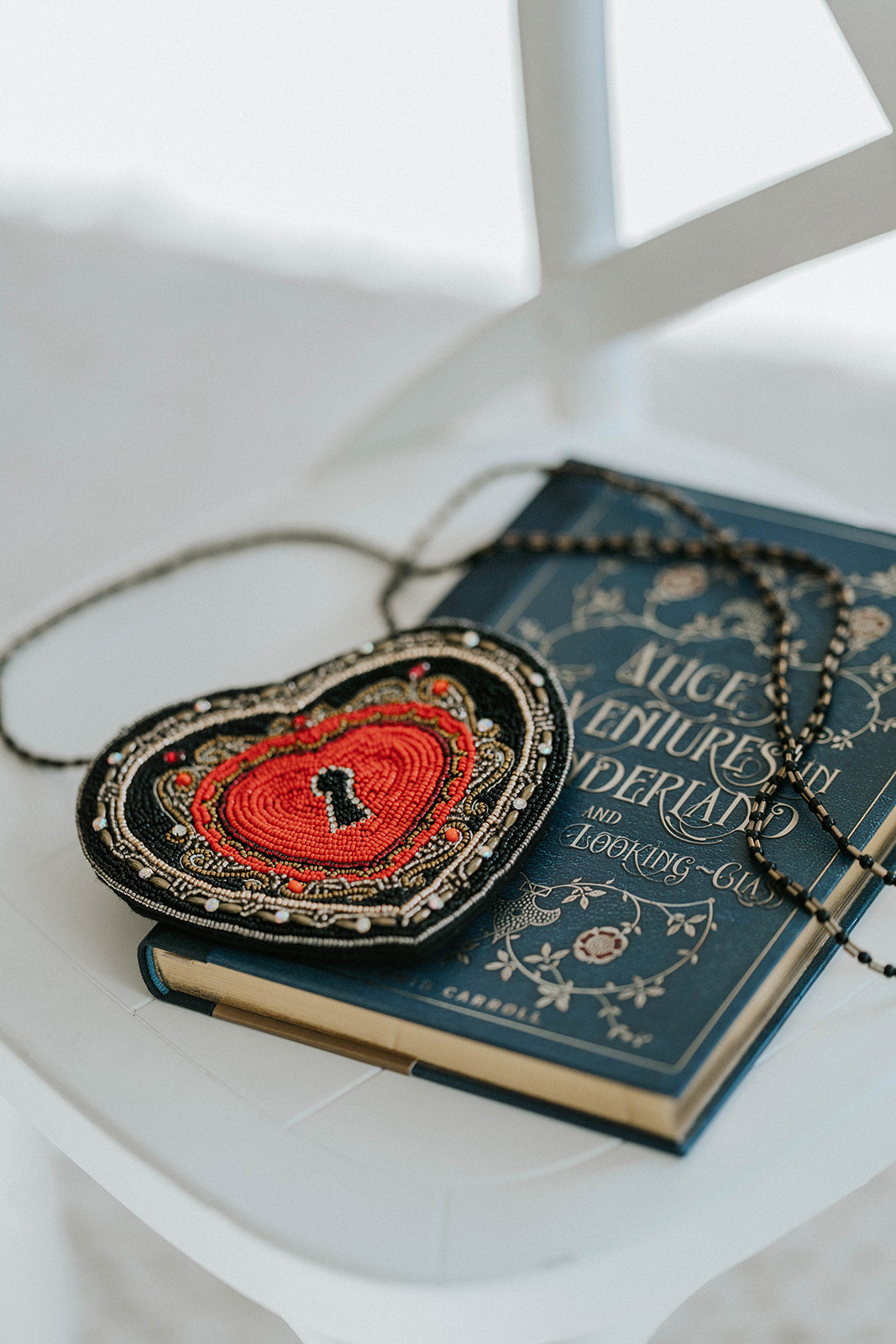 Beaded heart purse with red and black design, keyhole detail, and intricate gold stitching, styled with a white dress and blue tartan scarf for a fairytale holiday accessory look.

Gothic-inspired red heart handbag with keyhole motif and beadwork, worn by girl in winter outfit, perfect for Valentine’s Day, fairytale fashion, or themed photoshoots.

Close-up of a heart-shaped beaded purse with ornate swirls, pearl accents, and a romantic keyhole center, styled for girls or women who love storybook and fantas