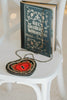Hand-beaded heart crossbody purse with red center and black trim, styled for gothic princess look with white bubble dress and navy tartan scarf, ideal for Valentine’s Day.

Girls fantasy handbag with keyhole embroidery and red beaded heart design, perfect for magical dress-up, boutique accessories, or romantic themed events.

Unique hand-beaded Valentine’s purse shaped like a heart with black and red seed beads, worn with a winter dress for holiday photo sessions or princess accessories.