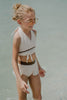 Toddler to tween girl in goddess-style cream bathing suit with halter neckline and high-waisted bottoms, standing on the shore

Girls neutral swimwear set featuring wrap halter top and soft mesh skirt, perfect for boho beachwear or summer shoots

Child in cream-colored two-piece swimsuit with wrap top and skirted bottom, posing barefoot in the sand on a sunny beach day