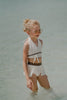 Boho-inspired cream girls swimsuit with wrap detail and side draping, styled for beach photos or summer vacation

Toddler to tween girl in goddess-style cream bathing suit with halter neckline and high-waisted bottoms, standing on the shore

Girls neutral swimwear set featuring wrap halter top and soft mesh skirt, perfect for boho beachwear or summer shoots

Child in cream-colored two-piece swimsuit with wrap top and skirted bottom, posing barefoot in the sand on a sunny beach day