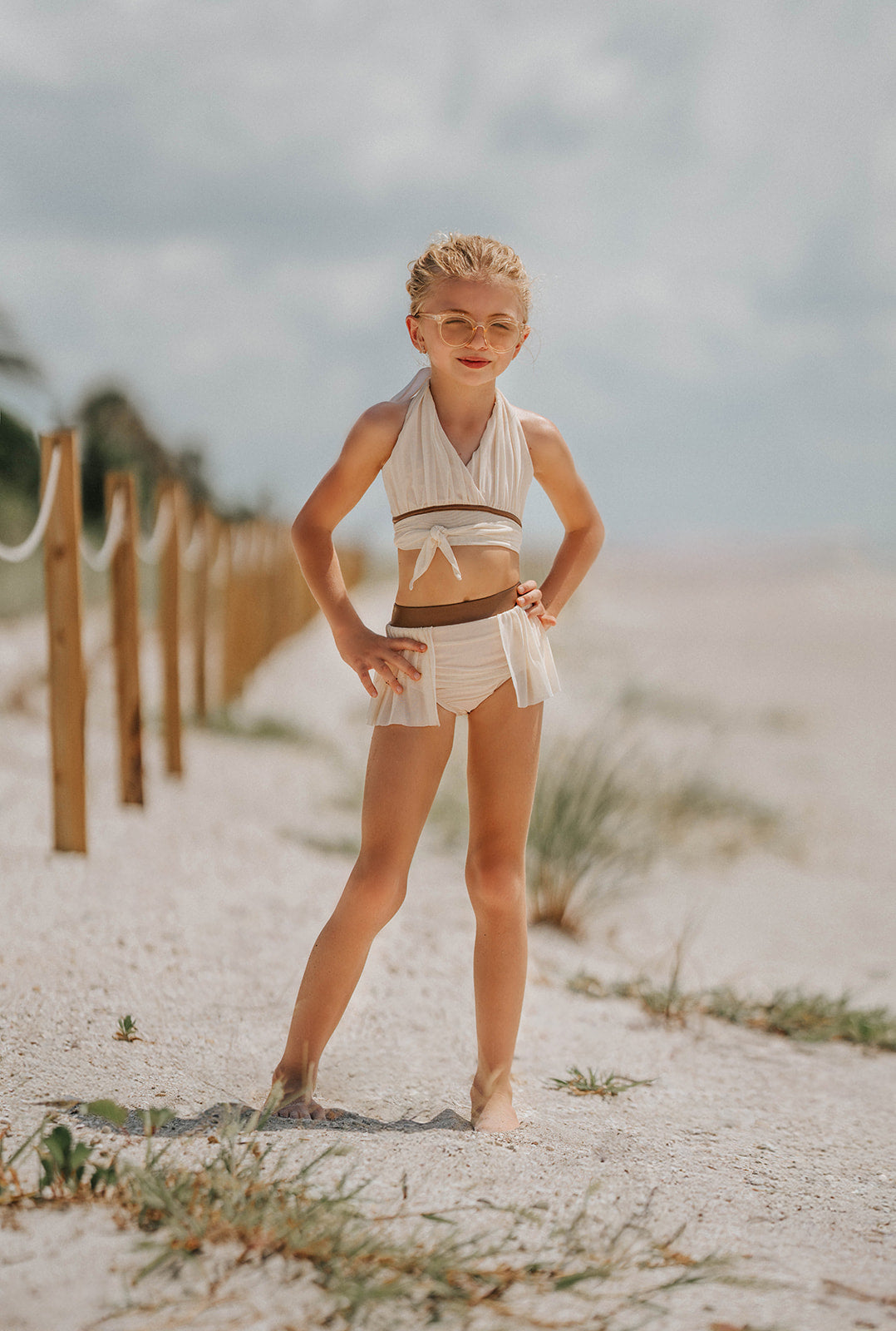 Girl wearing cream two-piece wrap swimsuit with halter top and flowy side skirt, posing confidently on a sandy beach

Boho-inspired cream girls swimsuit with wrap detail and side draping, styled for beach photos or summer vacation

Toddler to tween girl in goddess-style cream bathing suit with halter neckline and high-waisted bottoms, standing on the shore