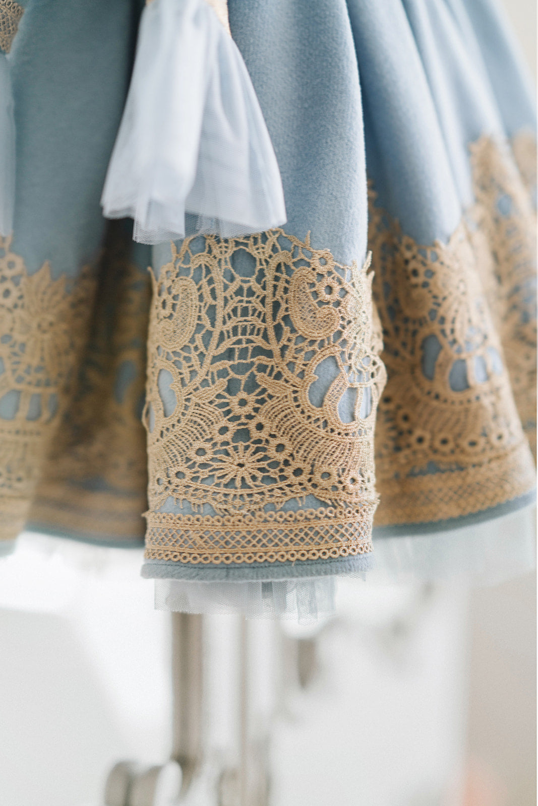 Victorian-inspired blue girls dress with gold embroidery, puff sleeves, and pearl buttons, perfect for birthdays or special occasions

Elegant heirloom girls dress in dusty blue with gold lace trim and tulle layers, hanging on ornate vintage-style mirror

Long sleeve blue and gold embroidered holiday dress for girls, featuring pearl buttons and layered tulle hem