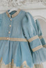 Victorian-inspired blue girls dress with gold embroidery, puff sleeves, and pearl buttons, perfect for birthdays or special occasions

Elegant heirloom girls dress in dusty blue with gold lace trim and tulle layers, hanging on ornate vintage-style mirror

Long sleeve blue and gold embroidered holiday dress for girls, featuring pearl buttons and layered tulle hem