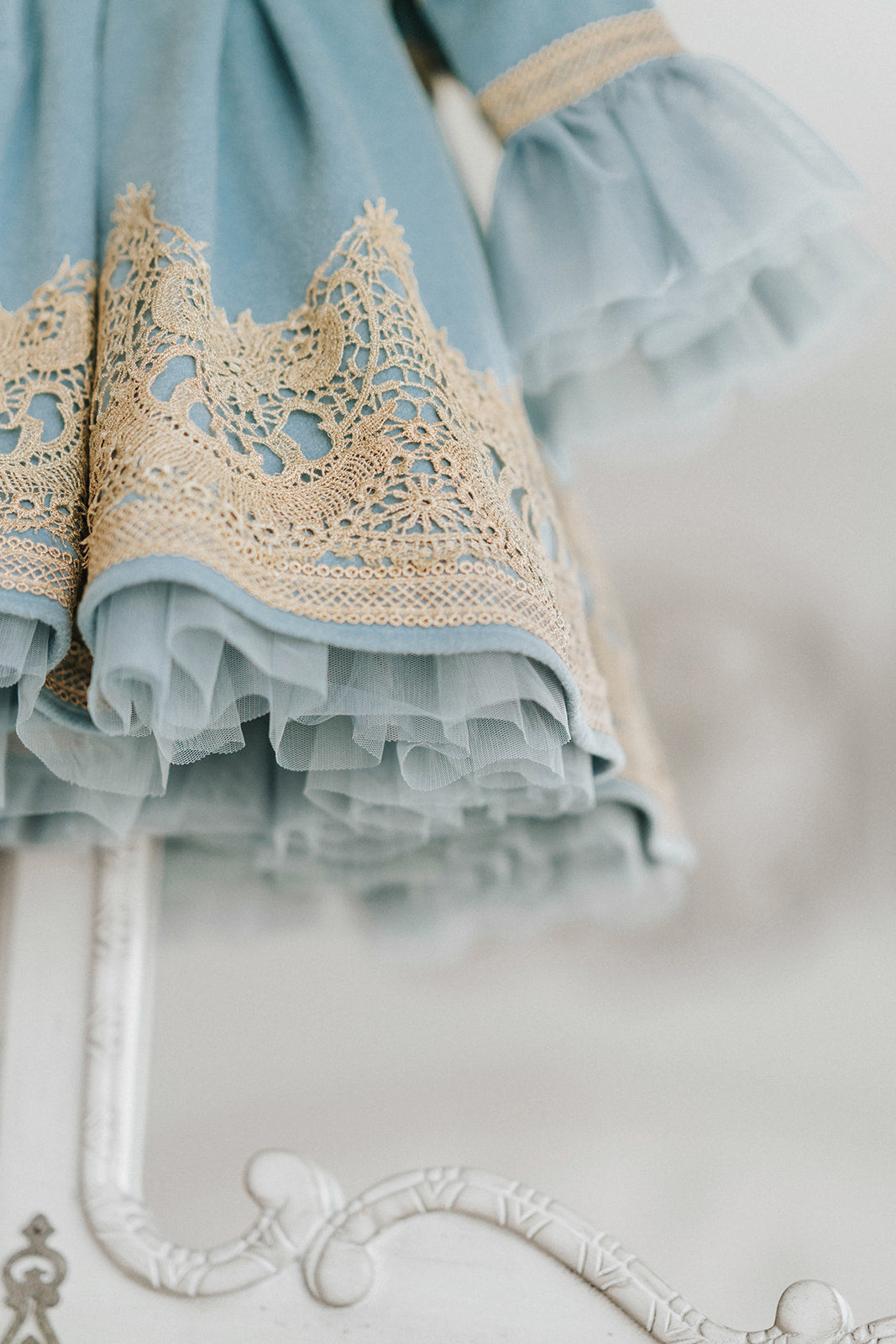 Elegant heirloom girls dress in dusty blue with gold lace trim and tulle layers, hanging on ornate vintage-style mirror

Long sleeve blue and gold embroidered holiday dress for girls, featuring pearl buttons and layered tulle hem

Girls vintage-style formal gown in soft blue with gold lace and flounce sleeves, ideal for portraits or weddings

Classic blue heirloom dress for toddlers and girls with ornate embroidery and pearl detailing, styled for a timeless photo shoot