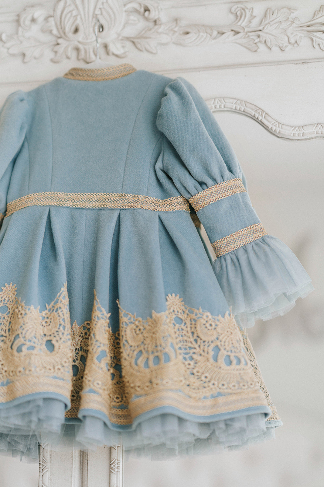 Elegant heirloom girls dress in dusty blue with gold lace trim and tulle layers, hanging on ornate vintage-style mirror

Long sleeve blue and gold embroidered holiday dress for girls, featuring pearl buttons and layered tulle hem

Girls vintage-style formal gown in soft blue with gold lace and flounce sleeves, ideal for portraits or weddings

Classic blue heirloom dress for toddlers and girls with ornate embroidery and pearl detailing, styled for a timeless photo shoot