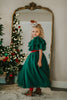 A young girl is wearing the Martha Ball Gown.  The queen anne neckline is adorned by an evergreen ruffles. The red swiss dot bodice leads into flowing evergreene tulle skirts.  