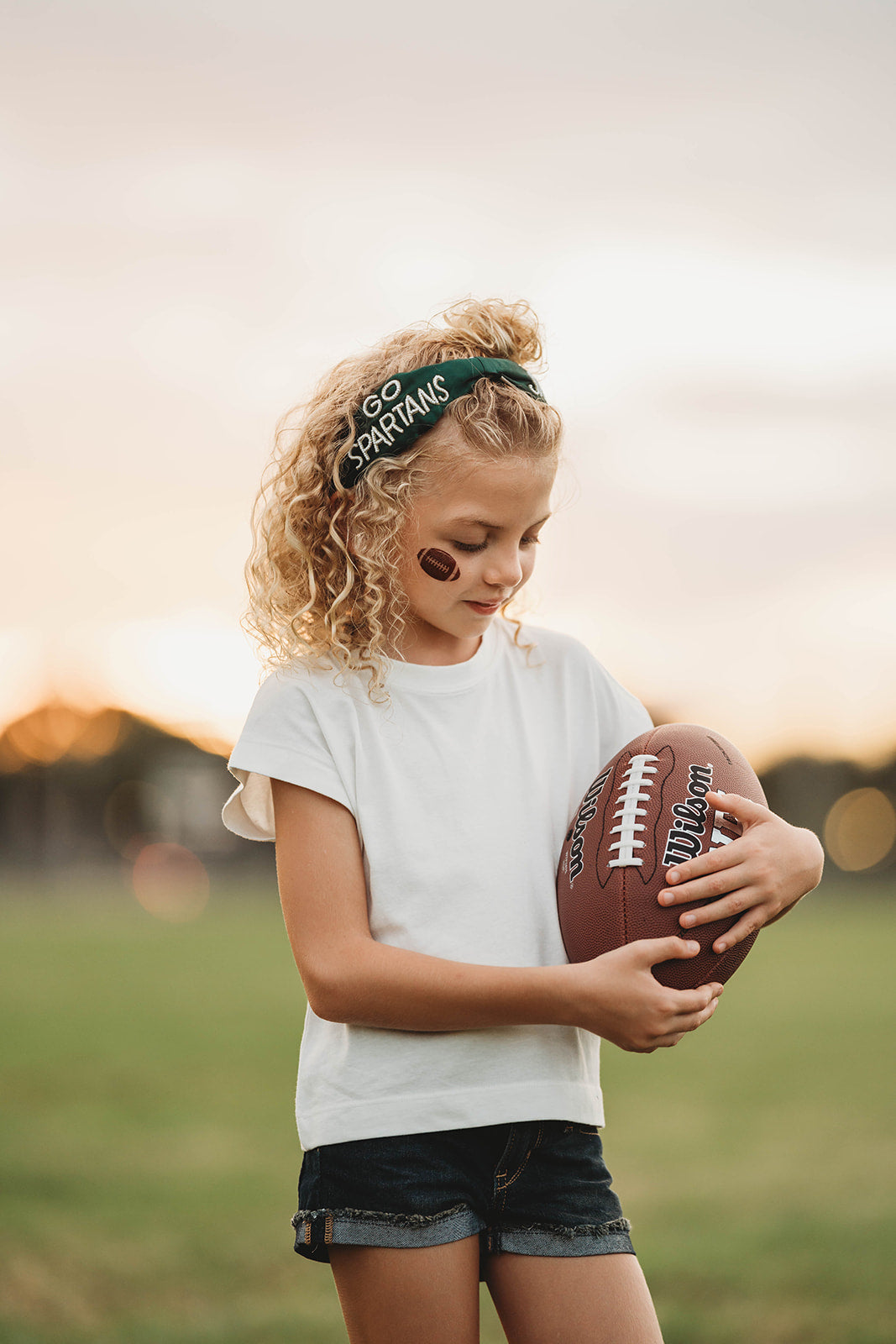 Girl wearing green “Go Spartans” headband holding a football on a grassy field at sunset, dressed in white tee and denim shorts

Child in team spirit outfit with green “Go Spartans” headband and football, perfect for game day or school pep rally

Little girl showing Spartan pride with beaded green headband and football, styled for fall sports or tailgate season

Girls football fan look with sparkly “Go Spartans” headband and casual outfit, standing in a field at golden hour