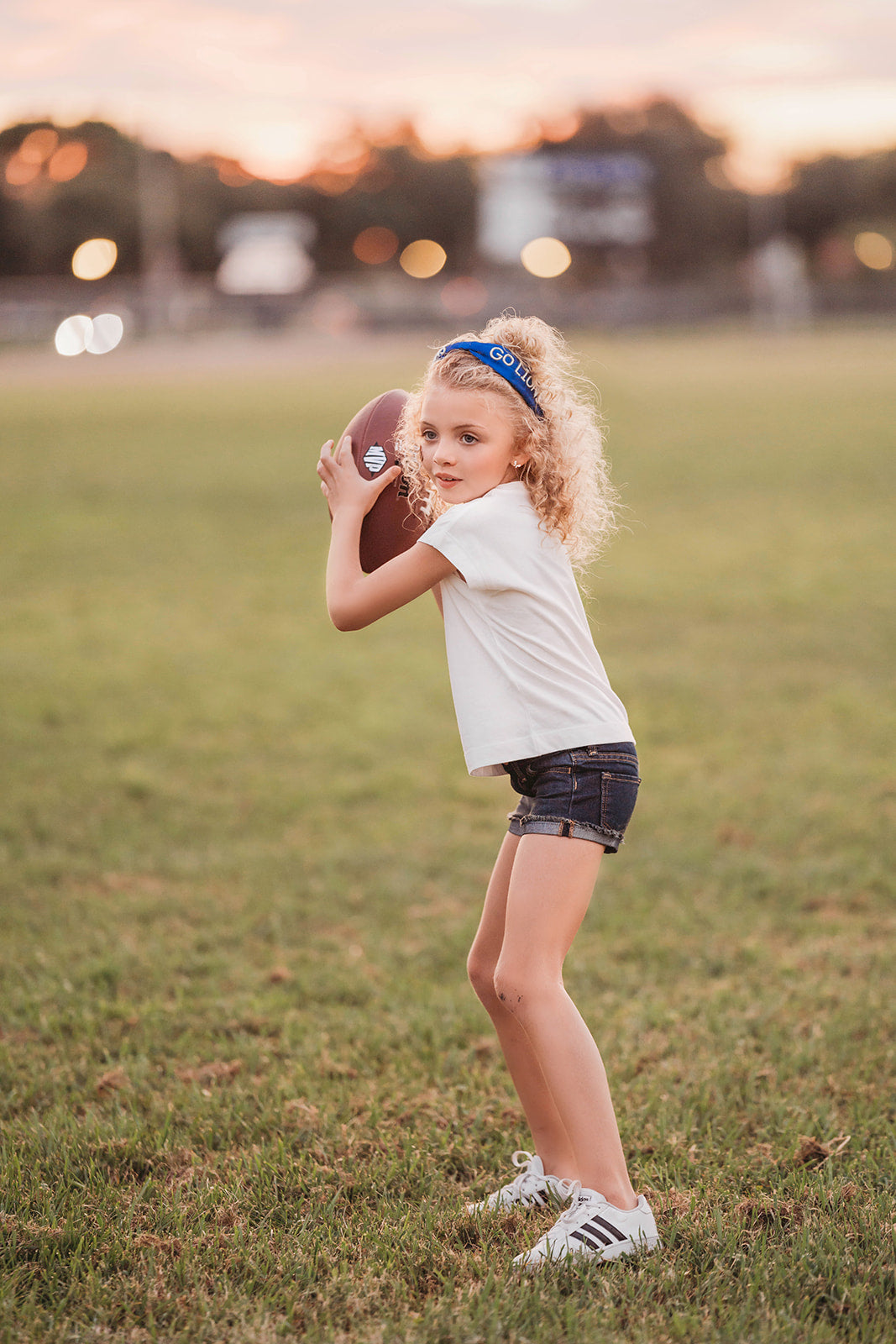 Girl wearing blue “Go Lions” headband holding football on a field at sunset, dressed in white tee and denim shorts

Child wearing sparkly blue team spirit headband that says “Go Lions,” styled with football face sticker and sporty outfit

Little girl showing team pride in “Go Lions” beaded headband while holding football during golden hour on the field

Girls football game day outfit with blue “Go Lions” headband and pigskin, perfect for team spirit wear or cheerleaders