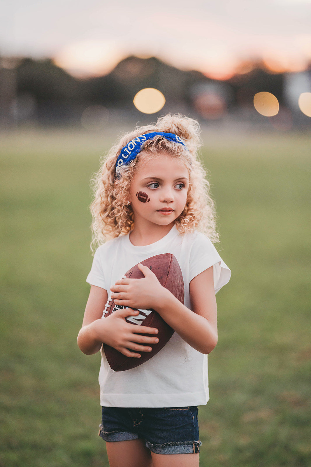 Girl wearing blue “Go Lions” headband holding football on a field at sunset, dressed in white tee and denim shorts

Child wearing sparkly blue team spirit headband that says “Go Lions,” styled with football face sticker and sporty outfit

Little girl showing team pride in “Go Lions” beaded headband while holding football during golden hour on the field

Girls football game day outfit with blue “Go Lions” headband and pigskin, perfect for team spirit wear or cheerleaders