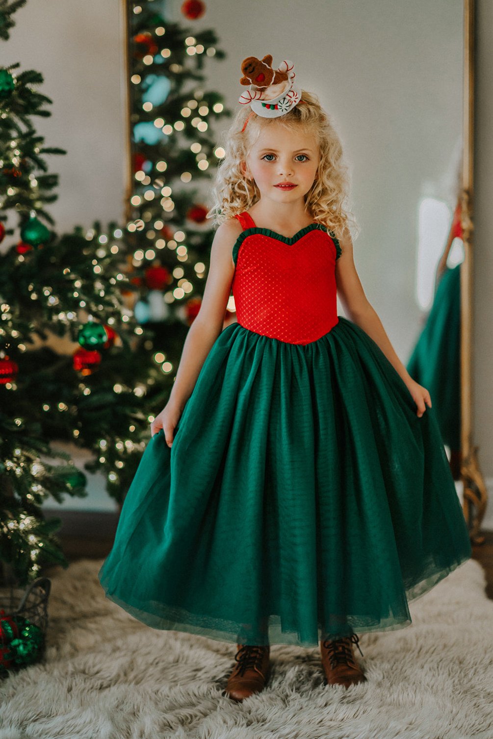 A young girl is wearing the Martha Ball Gown.  The queen anne neckline is adorned by an evergreen ruffles. The red swiss dot bodice leads into flowing evergreene tulle skirts.  