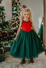 A young girl is wearing the Martha Ball Gown.  The queen anne neckline is adorned by an evergreen ruffles. The red swiss dot bodice leads into flowing evergreene tulle skirts.  