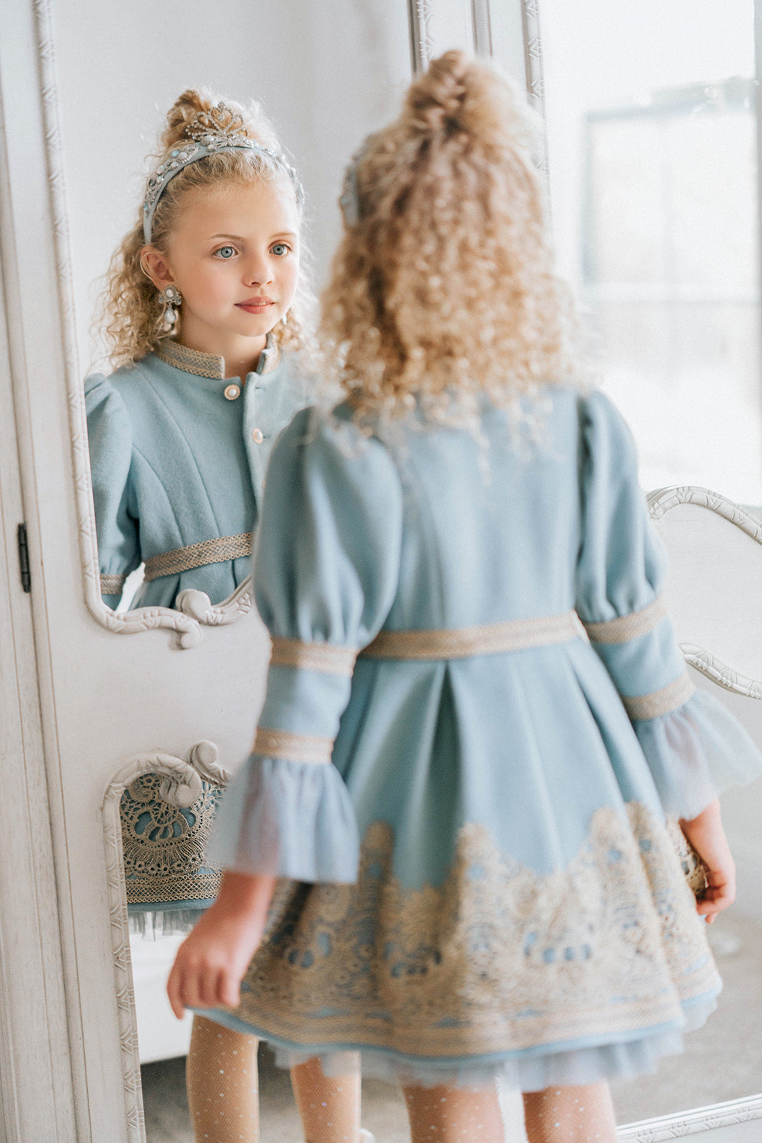 Victorian-inspired blue girls dress with gold embroidery, puff sleeves, and pearl buttons, perfect for birthdays or special occasions

Elegant heirloom girls dress in dusty blue with gold lace trim and tulle layers, hanging on ornate vintage-style mirror

Long sleeve blue and gold embroidered holiday dress for girls, featuring pearl buttons and layered tulle hem