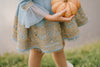 Victorian-inspired blue girls dress with gold embroidery, puff sleeves, and pearl buttons, perfect for birthdays or special occasions

Elegant heirloom girls dress in dusty blue with gold lace trim and tulle layers, hanging on ornate vintage-style mirror

Long sleeve blue and gold embroidered holiday dress for girls, featuring pearl buttons and layered tulle hem