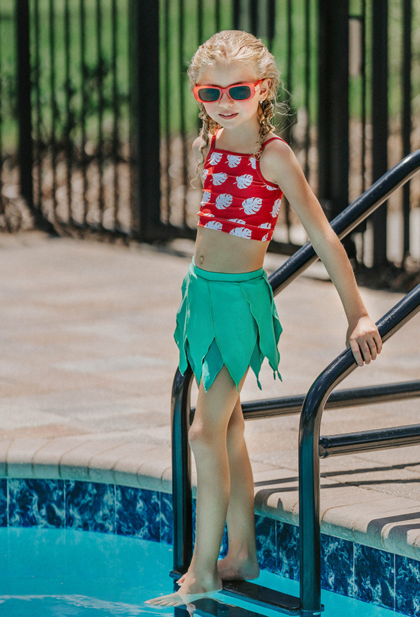 Girls Hawaiian swimsuit with bold red and white monstera top and green layered leaf swim skirt, perfect for beach or resort

Kid's luau-inspired two-piece swimsuit with monstera print top and leafy green skirt, styled with red sunglasses by the pool
