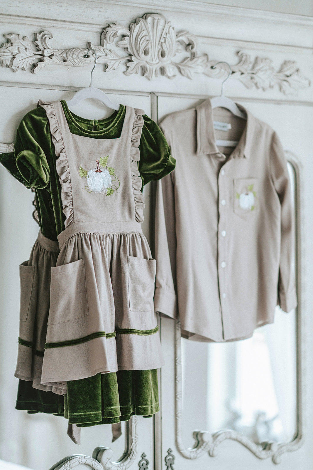 Girls green velvet dress with linen apron featuring embroidered pale blue pumpkin and ruffle trim, perfect for fall photos or Thanksgiving

Heirloom-style green velvet holiday dress with linen pinafore and pumpkin embroidery, styled for autumn or fairytale dress-up

Fall girls outfit with green velvet dress and embroidered pumpkin apron, hanging on vintage white carved mirror

Toddler to tween Thanksgiving dress with velvet base, apron pockets, and embroidered pumpkin design, ideal for family photos