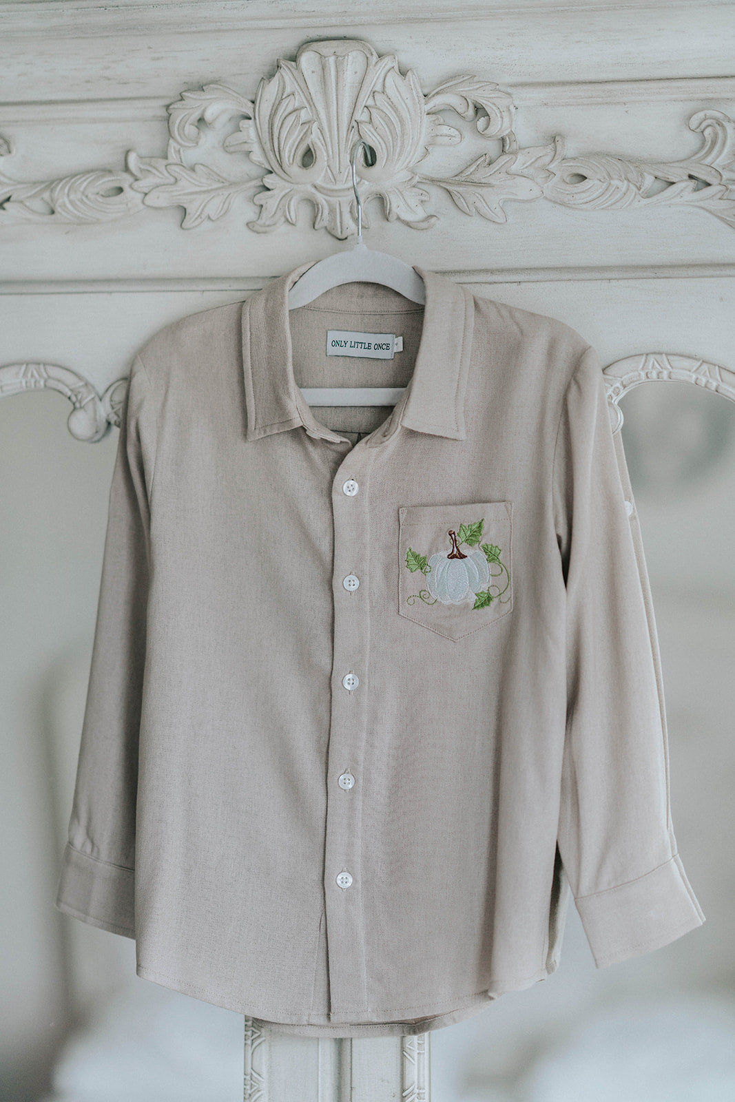 Boys beige button-up shirt with embroidered white pumpkin on chest pocket, hanging on vintage carved mirror for fall or Thanksgiving

Neutral boys fall shirt with embroidered pumpkin on pocket, styled for autumn photos, Thanksgiving, or sibling matching sets

Classic boys button-down shirt in light tan with embroidered blue pumpkin, perfect for harvest season or family portraits

Fall button-up shirt for toddlers and boys with embroidered pumpkin pocket detail, styled for Thanksgiving and heirloom outfits

