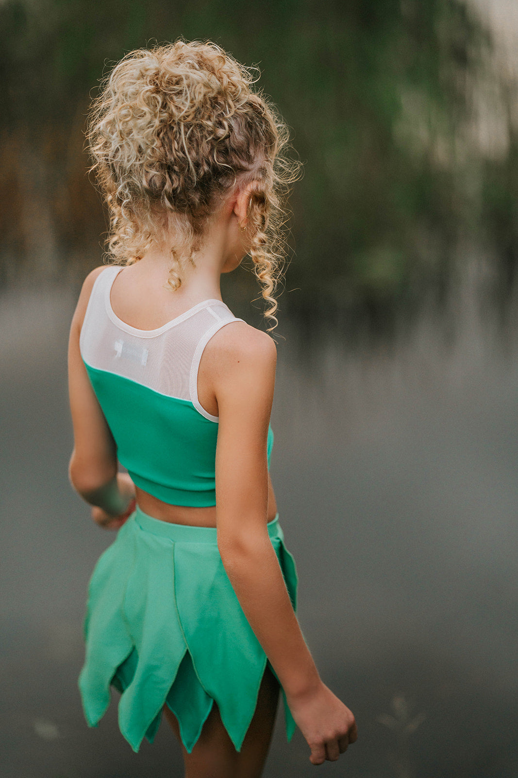 Child in green leaf skirt and matching top posing outdoors, perfect fairy or nature-themed costume for girls
