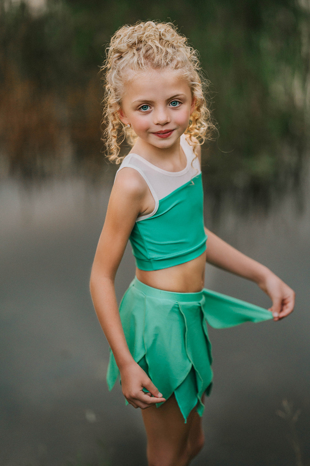 Young girl in a green and white dress standing by a body of water.