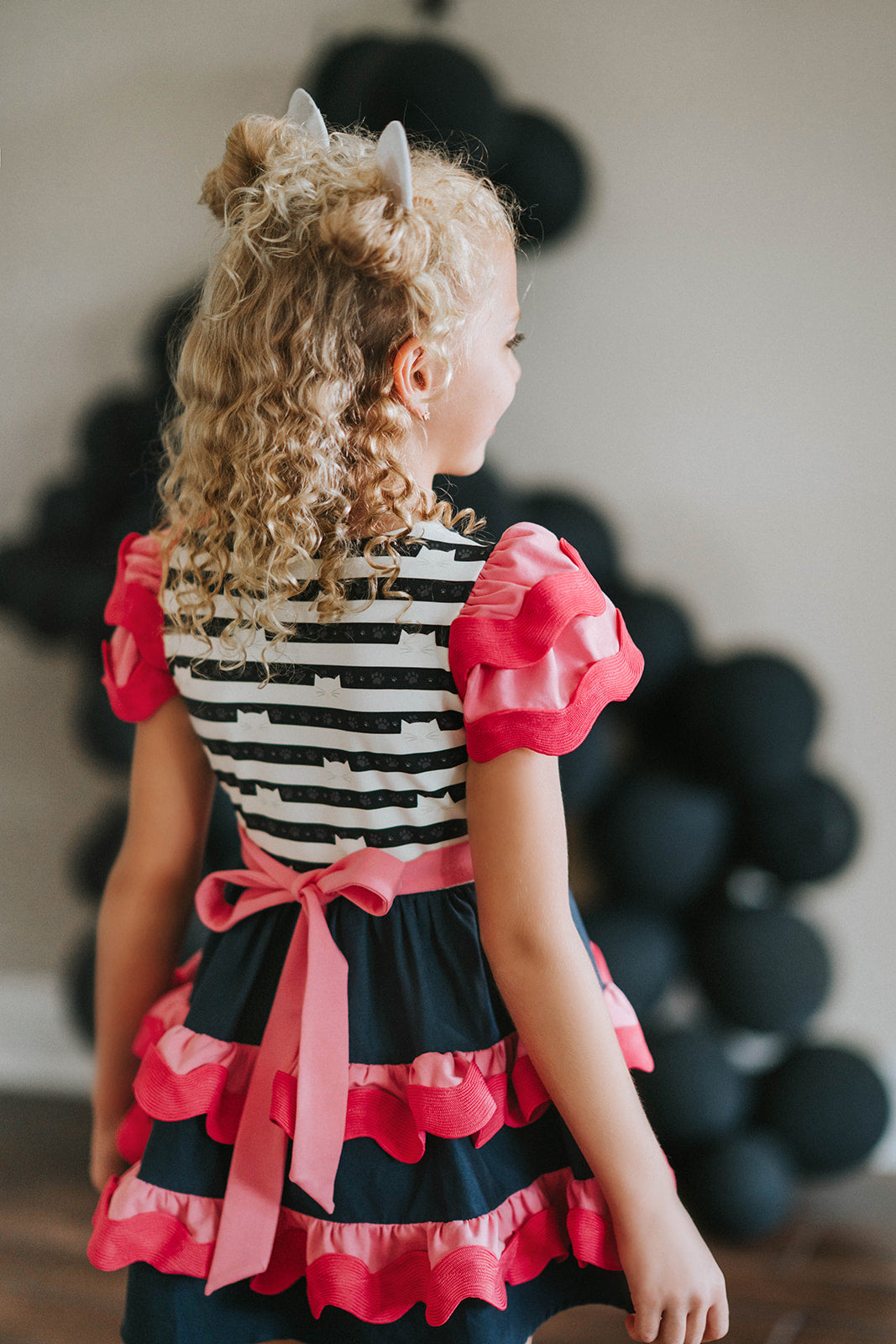 Girl wearing Gabby’s Dollhouse–inspired cat dress with pink and navy ruffles, striped kitty print bodice, and glitter cat ears

Girls ruffle party dress with black and white cat print top, pink waistband, and layered pink and navy skirt, styled for birthday

Gabby’s Dollhouse fan outfit featuring striped cat face bodice, double flutter sleeves, and tiered ruffle skirt for toddlers or girls

Child wearing a pink and navy cat-themed dress with kitty ears headband, perfect for dress-up, play, or themed birthda