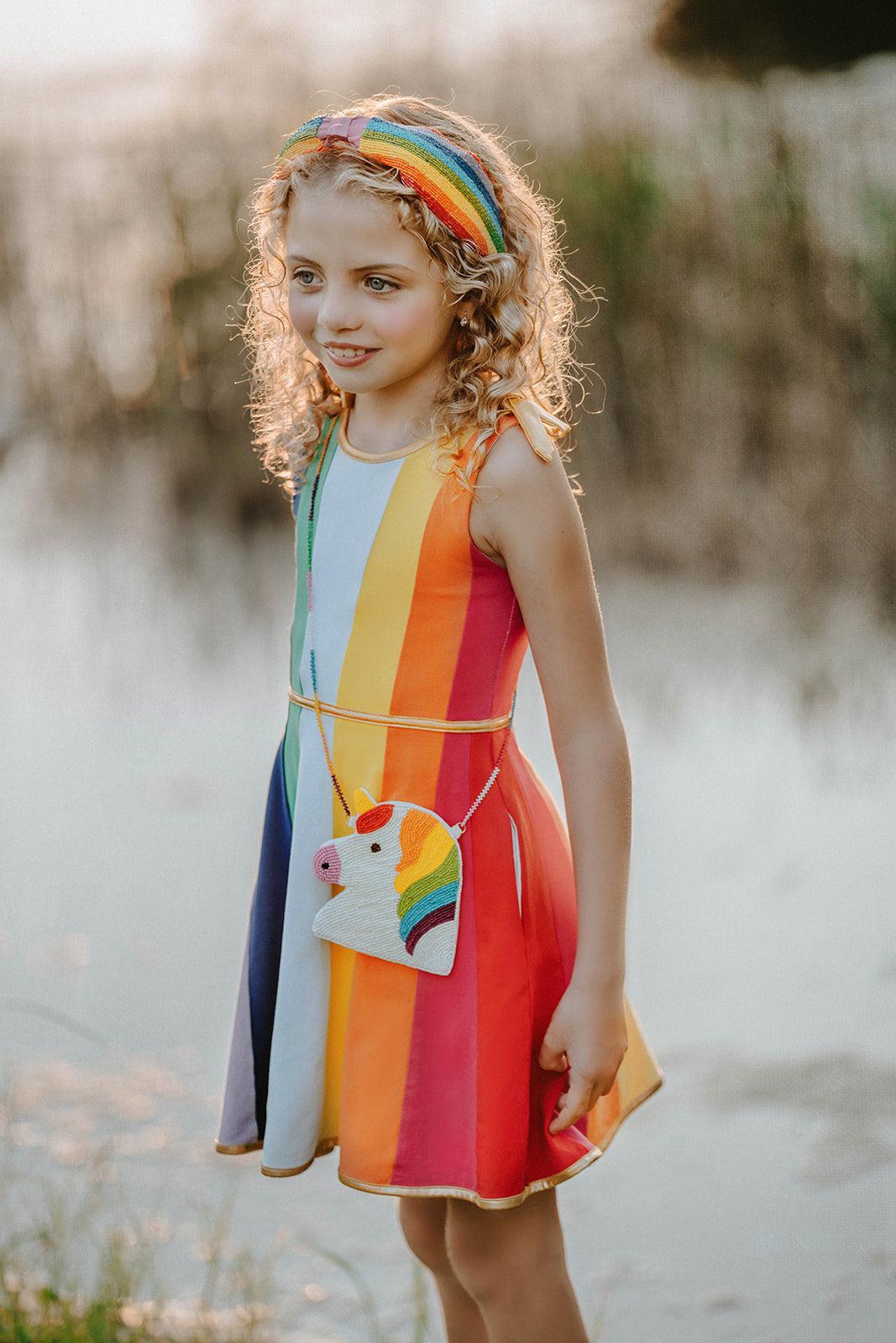 Beaded unicorn purse with rainbow mane and matching colorful strap displayed on a white chair next to a rainbow headband