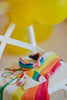 Colorful unicorn-themed party favors on a white surface with yellow balloons in the background.