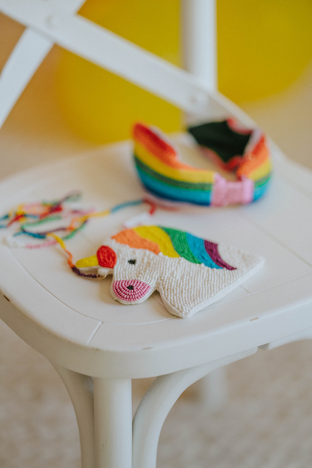 Rainbow unicorn-shaped beaded handbag for kids with colorful strap, shown with matching headband on chair