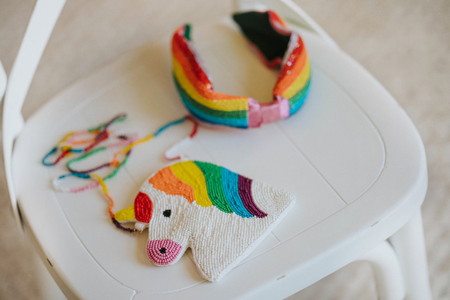 Rainbow unicorn-shaped beaded handbag for kids with colorful strap, shown with matching headband on chair