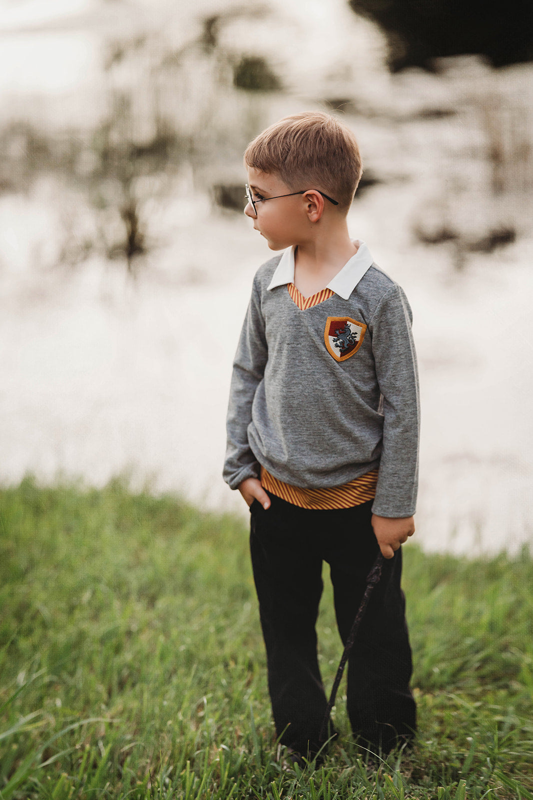 Young boy wearing wizard costume top with gold and red striped accents and crest patch, perfect for Halloween or dress-up

Wizard-themed boys shirt with collar and house crest, inspired by Harry Potter, styled for magical play or school events

Toddler boy in grey wizard top with white collar and Gryffindor-style crest, holding a wand and playing outside

Magical school uniform shirt for boys with embroidered crest and striped neckline, ideal for costumes or pretend play