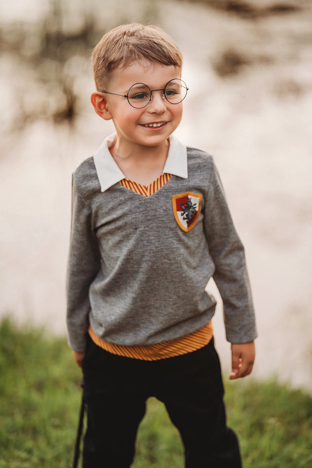 Toddler boy dressed in Gryffindor-inspired wizard shirt with crest and collar, holding wand and smiling outdoors

Young boy wearing wizard costume top with gold and red striped accents and crest patch, perfect for Halloween or dress-up

Wizard-themed boys shirt with collar and house crest, inspired by Harry Potter, styled for magical play or school events