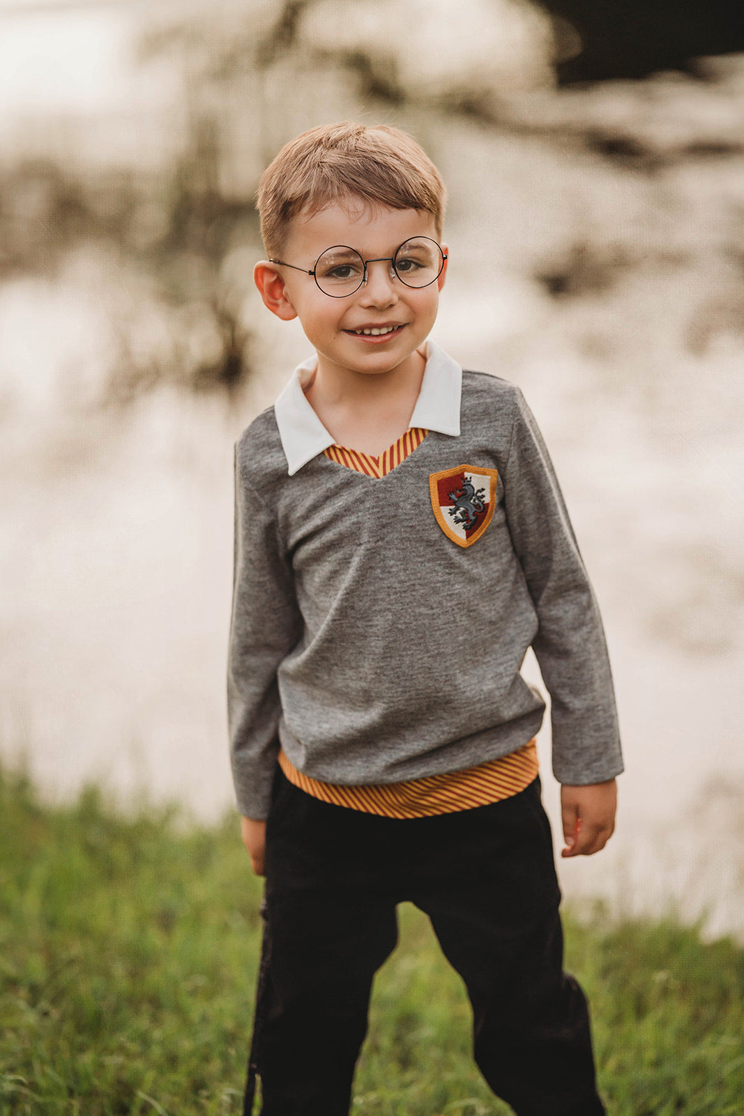 Young boy wearing wizard costume top with gold and red striped accents and crest patch, perfect for Halloween or dress-up

Wizard-themed boys shirt with collar and house crest, inspired by Harry Potter, styled for magical play or school events

Toddler boy in grey wizard top with white collar and Gryffindor-style crest, holding a wand and playing outside

Magical school uniform shirt for boys with embroidered crest and striped neckline, ideal for costumes or pretend play