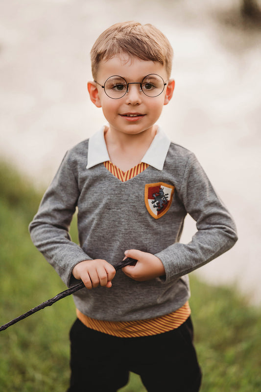 Toddler boy dressed in Gryffindor-inspired wizard shirt with crest and collar, holding wand and smiling outdoors

Young boy wearing wizard costume top with gold and red striped accents and crest patch, perfect for Halloween or dress-up

Wizard-themed boys shirt with collar and house crest, inspired by Harry Potter, styled for magical play or school events