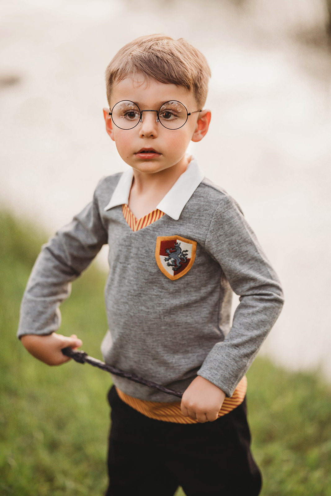 Young boy wearing wizard costume top with gold and red striped accents and crest patch, perfect for Halloween or dress-up

Wizard-themed boys shirt with collar and house crest, inspired by Harry Potter, styled for magical play or school events

Toddler boy in grey wizard top with white collar and Gryffindor-style crest, holding a wand and playing outside

Magical school uniform shirt for boys with embroidered crest and striped neckline, ideal for costumes or pretend play
