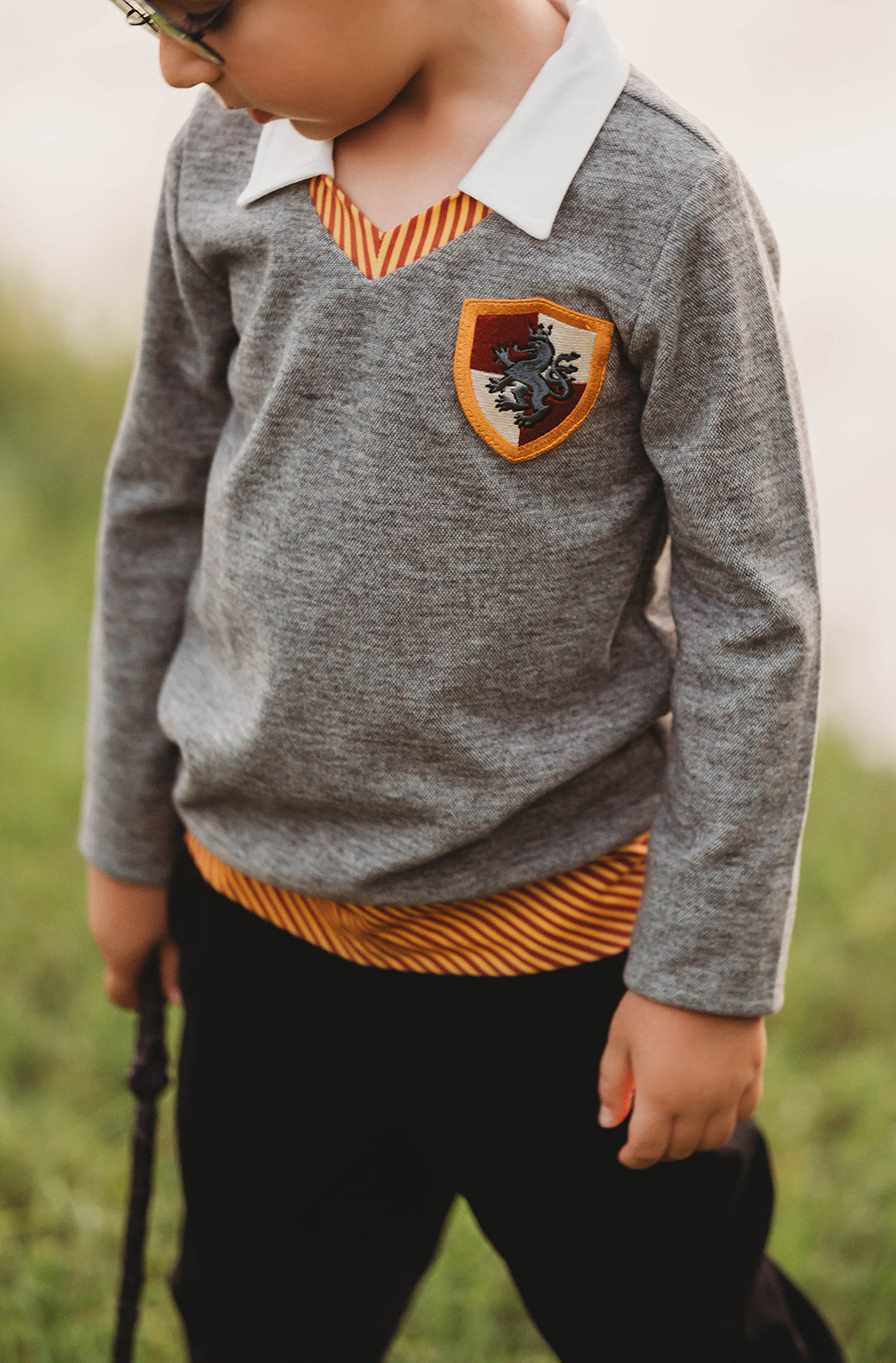 Toddler boy dressed in Gryffindor-inspired wizard shirt with crest and collar, holding wand and smiling outdoors

Young boy wearing wizard costume top with gold and red striped accents and crest patch, perfect for Halloween or dress-up

Wizard-themed boys shirt with collar and house crest, inspired by Harry Potter, styled for magical play or school events