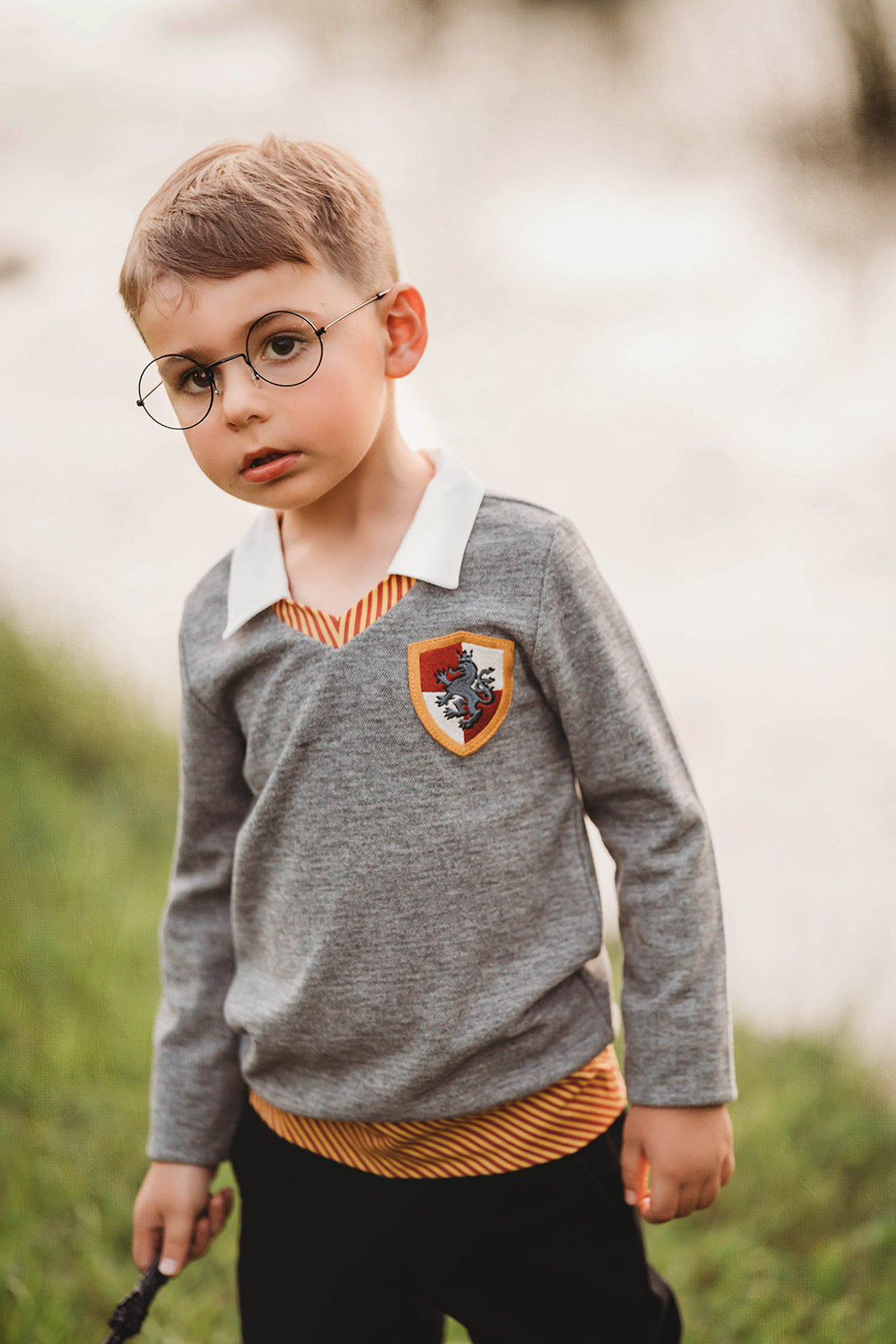 Young boy wearing wizard costume top with gold and red striped accents and crest patch, perfect for Halloween or dress-up

Wizard-themed boys shirt with collar and house crest, inspired by Harry Potter, styled for magical play or school events

Toddler boy in grey wizard top with white collar and Gryffindor-style crest, holding a wand and playing outside

Magical school uniform shirt for boys with embroidered crest and striped neckline, ideal for costumes or pretend play