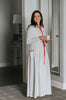 Woman wearing long white holiday nightgown with red trim, tie waist, and buttons, holding a teacup and smiling in a cozy morning setting, perfect for Christmas sleepwear.

White women's nightgown with red piping and buttons, styled with pockets and a tie waist, perfect for winter lounging, Christmas morning, or cozy holiday gift giving.

Adult holiday sleepwear for women featuring red contrast trim, full length, and soft knit fabric, styled with coffee cup in a warm, elegant home setting.