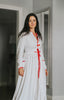 Woman wearing long white holiday nightgown with red trim, tie waist, and buttons, holding a teacup and smiling in a cozy morning setting, perfect for Christmas sleepwear.

White women's nightgown with red piping and buttons, styled with pockets and a tie waist, perfect for winter lounging, Christmas morning, or cozy holiday gift giving.

Adult holiday sleepwear for women featuring red contrast trim, full length, and soft knit fabric, styled with coffee cup in a warm, elegant home setting.