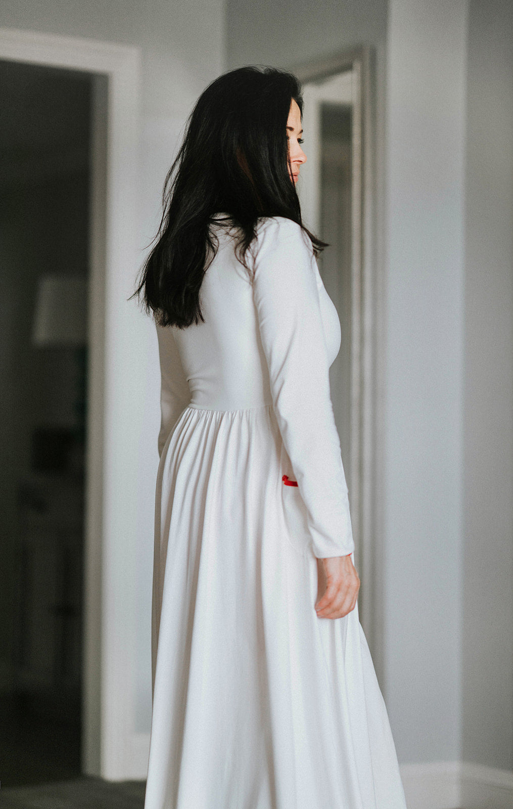 Woman wearing long white holiday nightgown with red trim, tie waist, and buttons, holding a teacup and smiling in a cozy morning setting, perfect for Christmas sleepwear.

White women's nightgown with red piping and buttons, styled with pockets and a tie waist, perfect for winter lounging, Christmas morning, or cozy holiday gift giving.

Adult holiday sleepwear for women featuring red contrast trim, full length, and soft knit fabric, styled with coffee cup in a warm, elegant home setting.