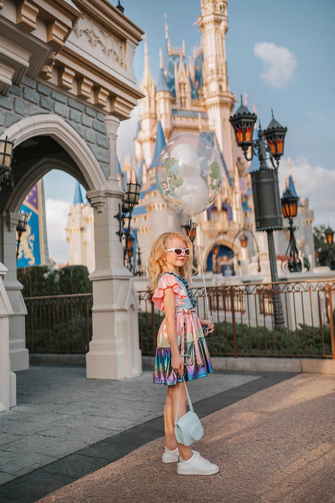 A vibrant metallic gown with colors of the rainbow. Pink flutter sleeves, tiered skirt perfect for twirling and a belted sash for that extra pizazz. 