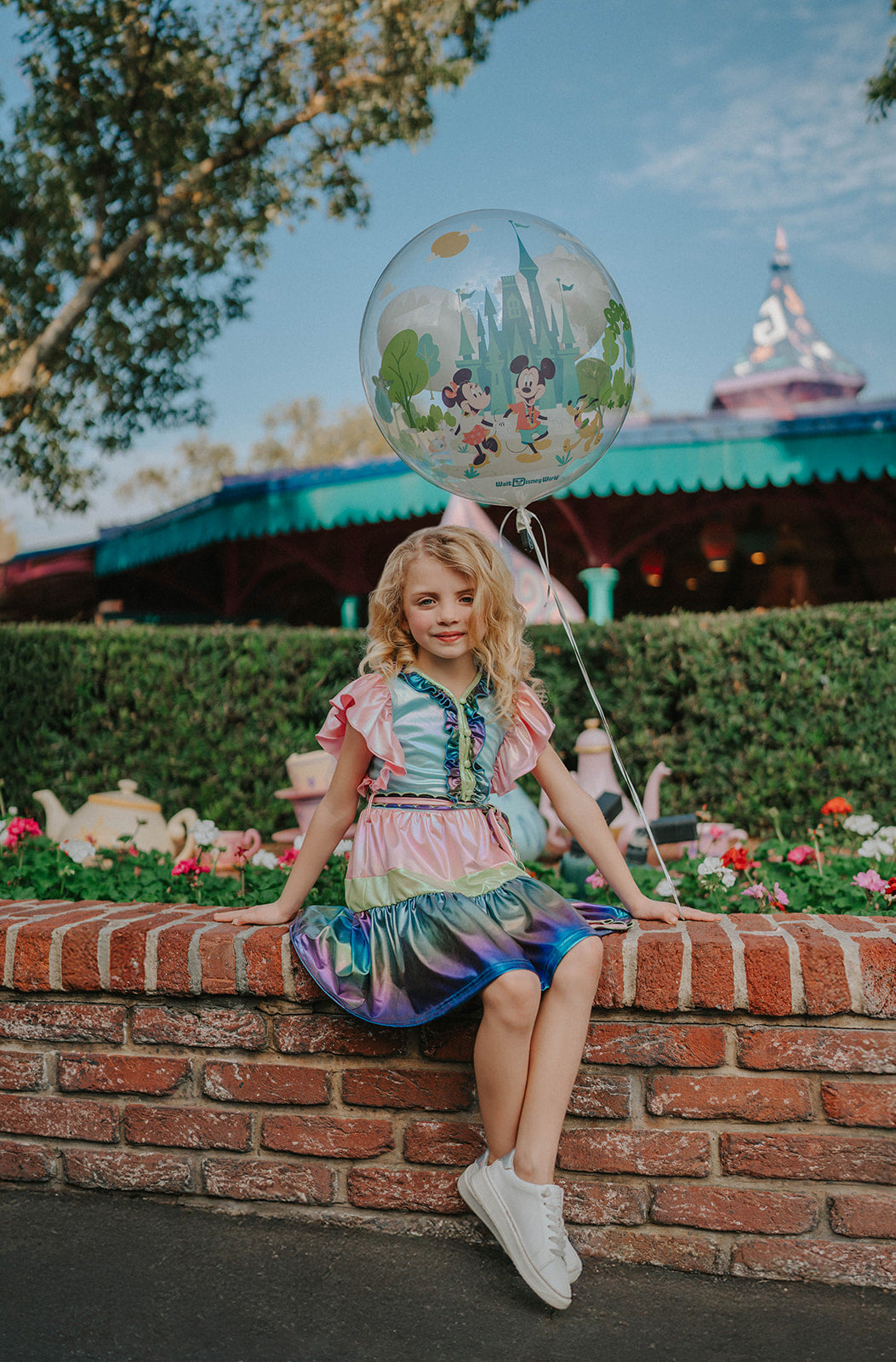 A vibrant metallic gown with colors of the rainbow. Pink flutter sleeves, tiered skirt perfect for twirling and a belted sash for that extra pizazz. 