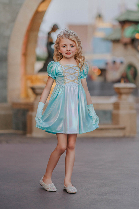 A young girls is wearing a metallic Cinderella Twirl dress. The light blue and white knee length dress has a criss cross gold ribbon across the bodice. The ballroom puff sleeves add elegance.