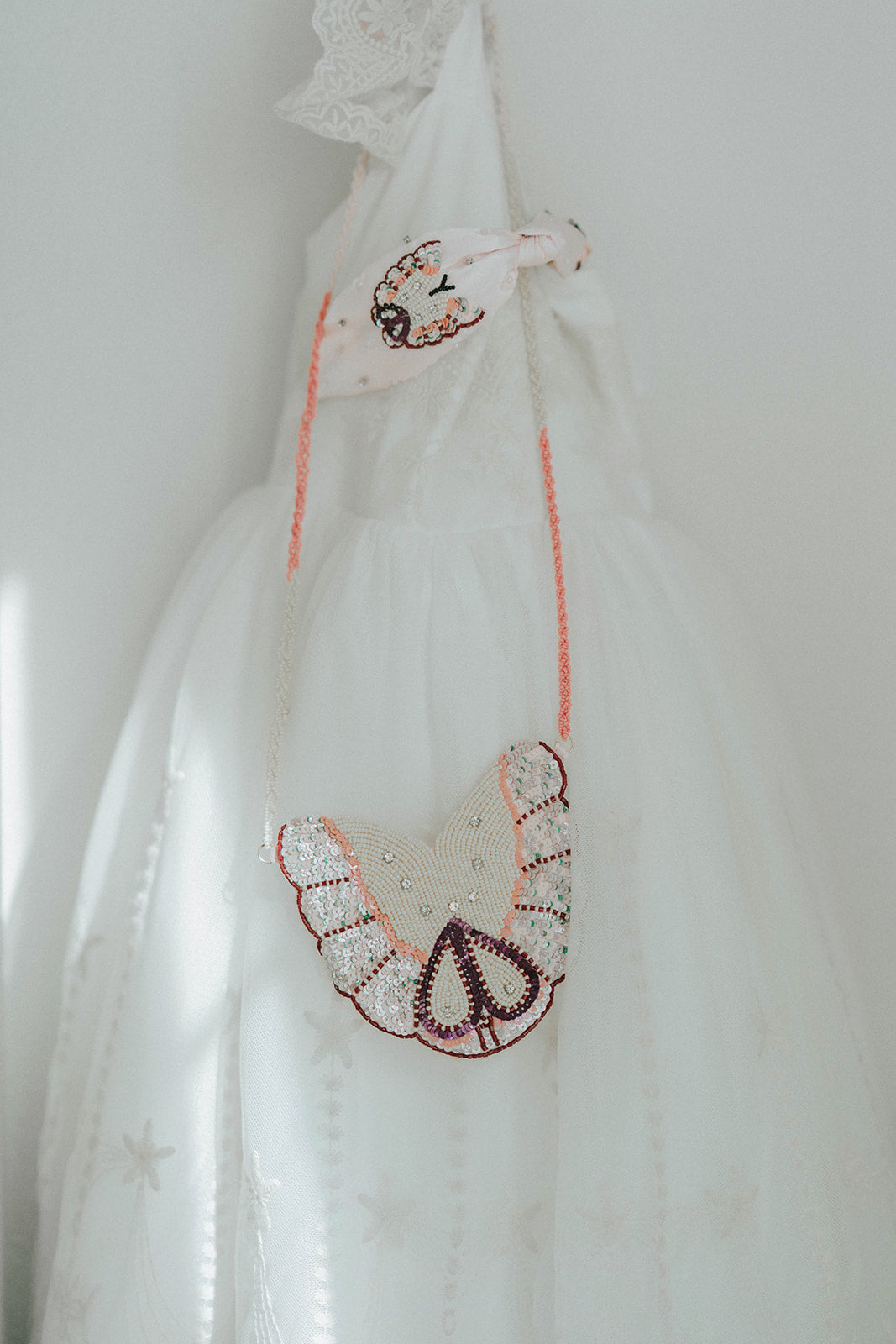 Close-up of a white and pink beaded butterfly purse with sequins, worn over a white tulle flower girl dress

Girls’ butterfly-shaped beaded purse with sequin wings and pink strap, styled with an elegant white dress

Delicate butterfly crossbody purse with beaded wings and sparkle detail, perfect for dress-up or special occasions

Iridescent butterfly beaded bag hanging from a girl's shoulder, styled with embroidered white gown