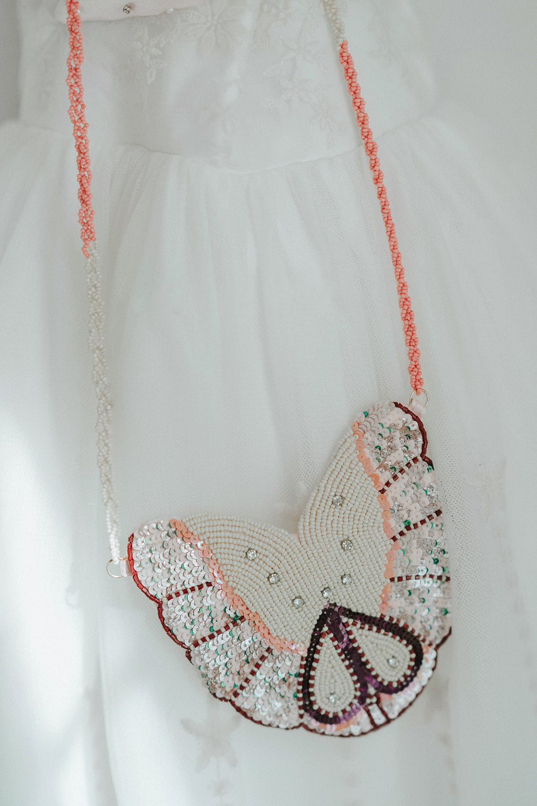 Girls’ butterfly-shaped beaded purse with sequin wings and pink strap, styled with an elegant white dress

Delicate butterfly crossbody purse with beaded wings and sparkle detail, perfect for dress-up or special occasions

Iridescent butterfly beaded bag hanging from a girl's shoulder, styled with embroidered white gown

Whimsical sequin butterfly purse for girls with pink and pearl beading, ideal for weddings or birthday dress-up