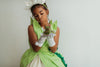 A young girl is wearing a beautiful bright green gown.  The layers on the bodice and skirt are cut like leaves.  There is a light yellow golden tulle skirt.   There is a magnolia flower with green leaves adorned on the side. 